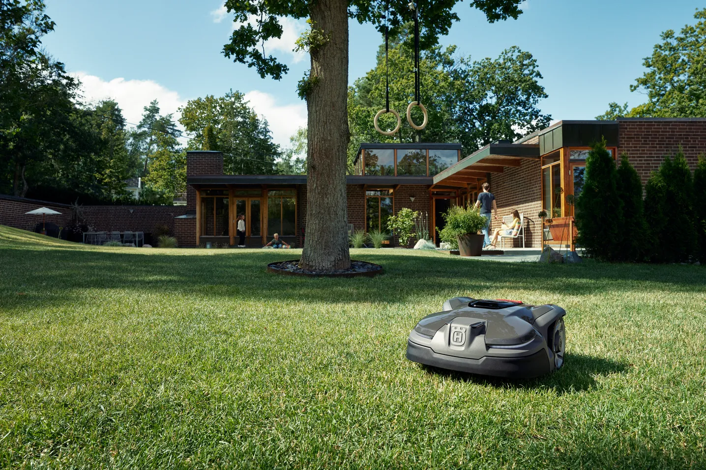 Robot cortacésped funcionando en un jardín con una casa moderna al fondo.